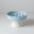 Blue ceramic elevated pet bowl with a slow-feeding surface and an anti-slip base