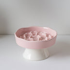 Pink ceramic slow feeder bowl with a raised base that lifts food up off the floor